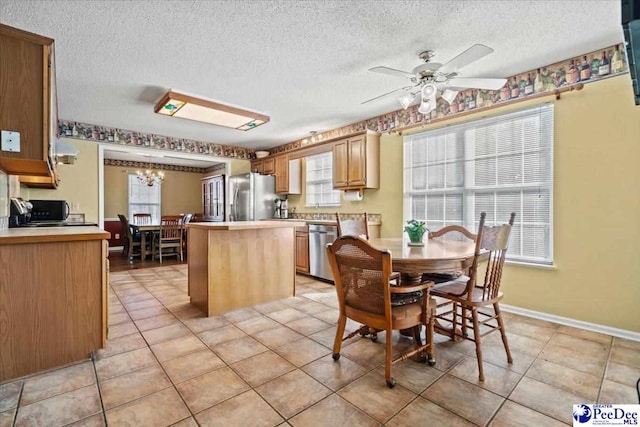 kitchen featuring a kitchen island, ceiling fan with notable chandelier, light tile patterned floors, stainless steel appliances, and a textured ceiling