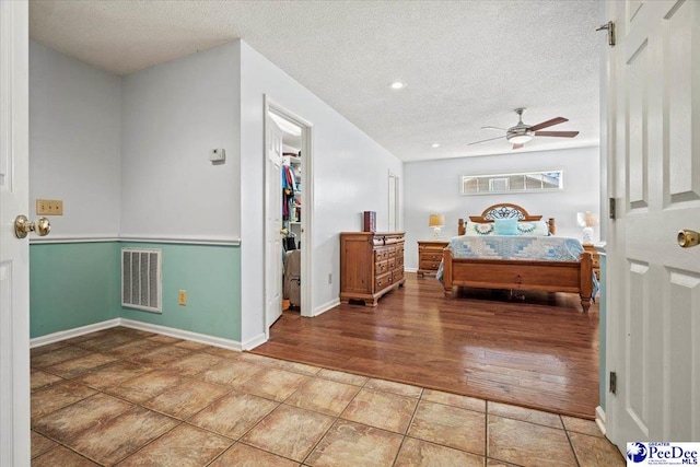 bedroom with tile patterned floors, a walk in closet, a textured ceiling, a closet, and ceiling fan