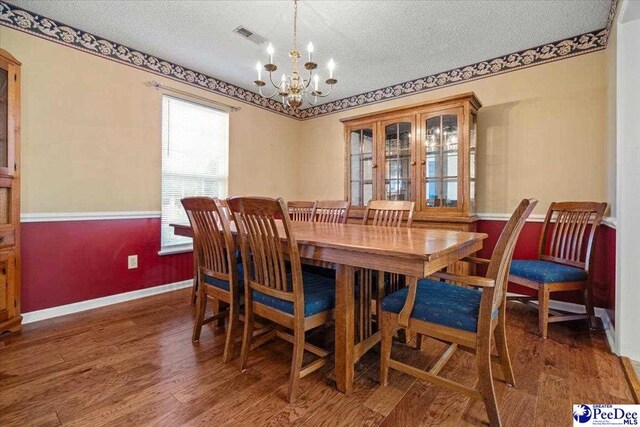 dining space featuring dark wood-type flooring, a chandelier, and a textured ceiling