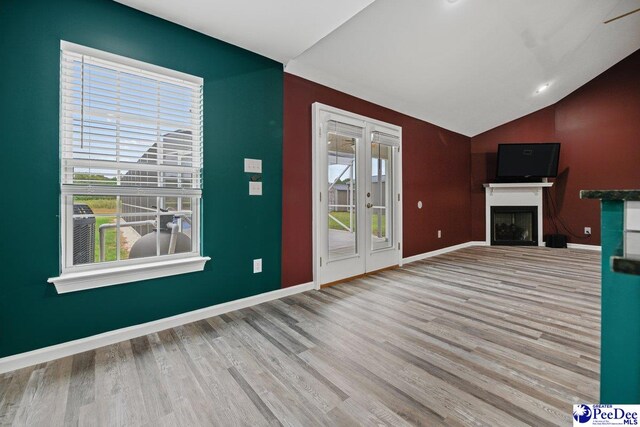 unfurnished living room featuring french doors, vaulted ceiling, and light wood-type flooring