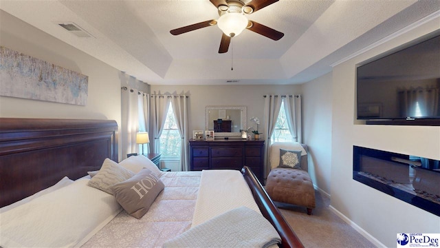 carpeted bedroom featuring a raised ceiling, ceiling fan, and multiple windows