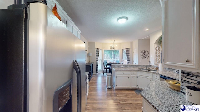 kitchen with sink, stainless steel refrigerator, kitchen peninsula, light hardwood / wood-style floors, and white cabinets