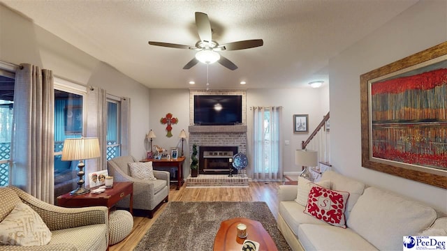 living room featuring hardwood / wood-style flooring, ceiling fan, a brick fireplace, and a textured ceiling