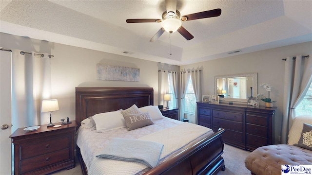 bedroom with light carpet, ceiling fan, a raised ceiling, and a textured ceiling