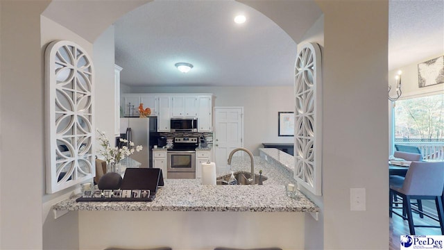 kitchen with sink, light stone counters, kitchen peninsula, stainless steel appliances, and white cabinets