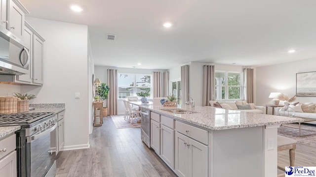 kitchen with sink, light hardwood / wood-style flooring, a breakfast bar, appliances with stainless steel finishes, and an island with sink