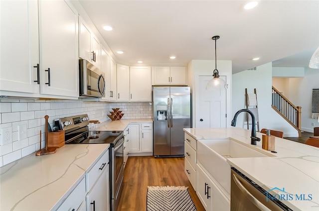 kitchen with light hardwood / wood-style floors, white cabinetry, hanging light fixtures, and stainless steel appliances