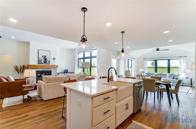 kitchen featuring decorative light fixtures, a breakfast bar, wood-type flooring, an island with sink, and stainless steel dishwasher