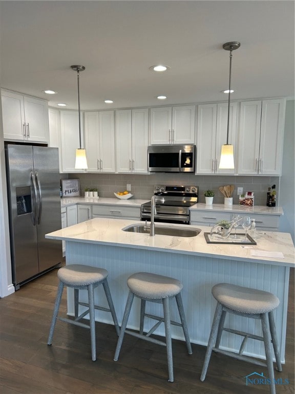 kitchen with appliances with stainless steel finishes, white cabinets, dark hardwood / wood-style floors, pendant lighting, and light stone countertops