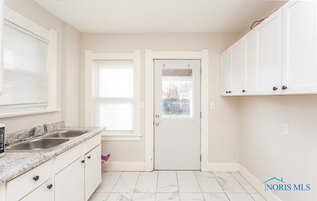 kitchen featuring white cabinets, light tile flooring, light stone counters, and sink