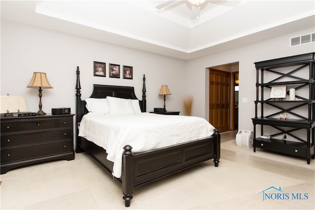 bedroom with ceiling fan, light colored carpet, and a tray ceiling