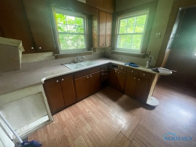 kitchen featuring kitchen peninsula, light wood-type flooring, sink, and dark brown cabinetry