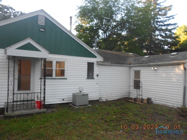 rear view of property with central AC unit and a yard