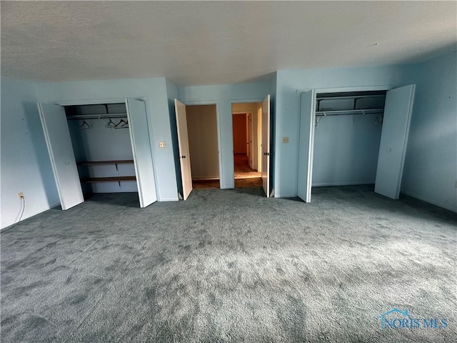 unfurnished bedroom with dark colored carpet and multiple closets