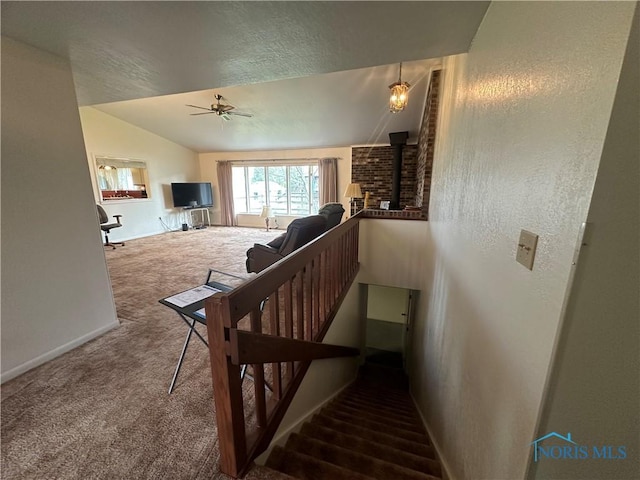 stairs with carpet floors, a wood stove, ceiling fan, and lofted ceiling