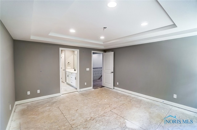 unfurnished bedroom with ensuite bathroom and a raised ceiling