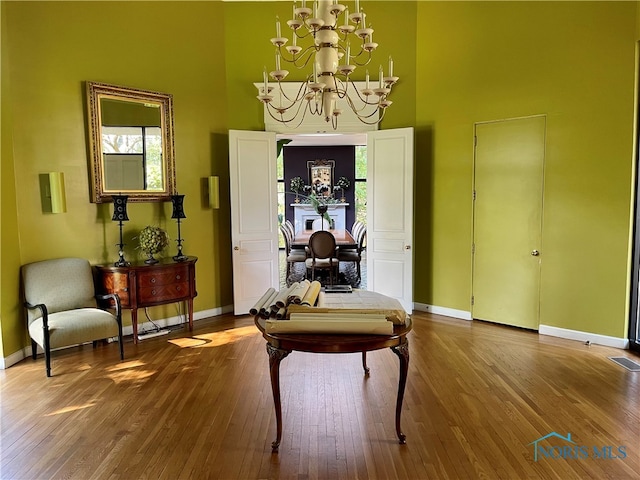 sitting room featuring a towering ceiling, hardwood / wood-style flooring, and an inviting chandelier