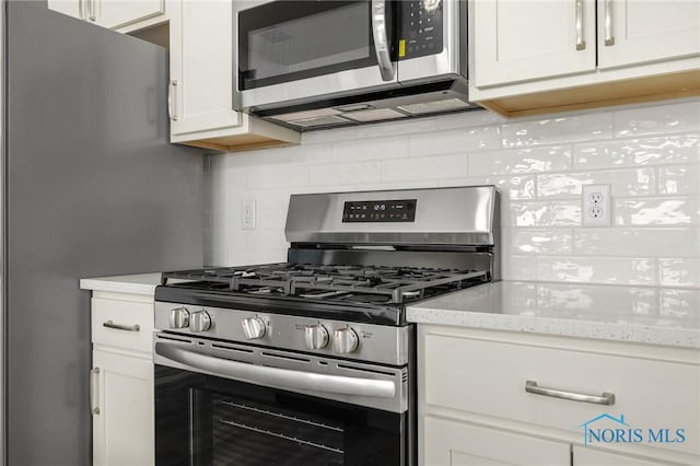 kitchen with light stone countertops, appliances with stainless steel finishes, white cabinets, and backsplash