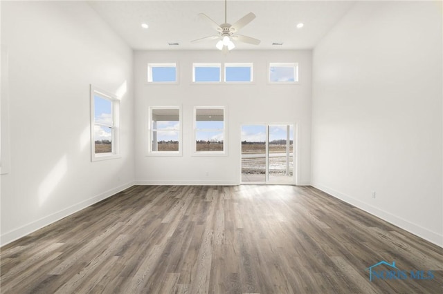 unfurnished living room featuring dark wood-type flooring, ceiling fan, and a towering ceiling