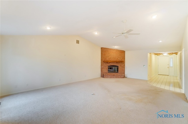 unfurnished living room featuring lofted ceiling, light colored carpet, a brick fireplace, and ceiling fan