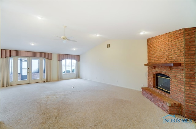 unfurnished living room featuring ceiling fan, a fireplace, brick wall, vaulted ceiling, and light colored carpet