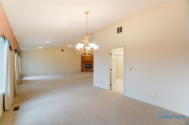 carpeted spare room with a fireplace, a chandelier, and vaulted ceiling