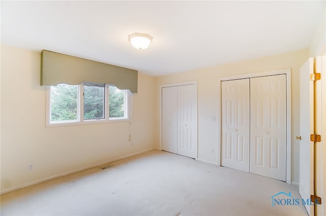 unfurnished bedroom with light carpet and multiple closets