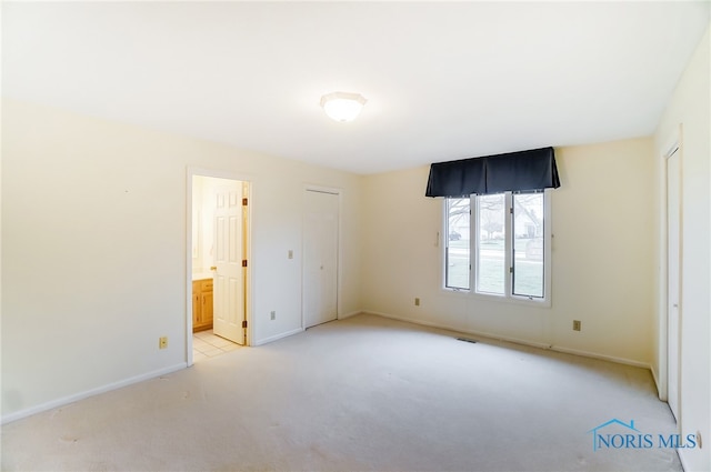 unfurnished bedroom featuring light carpet and ensuite bathroom