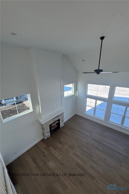 unfurnished living room featuring a stone fireplace, dark hardwood / wood-style floors, and ceiling fan