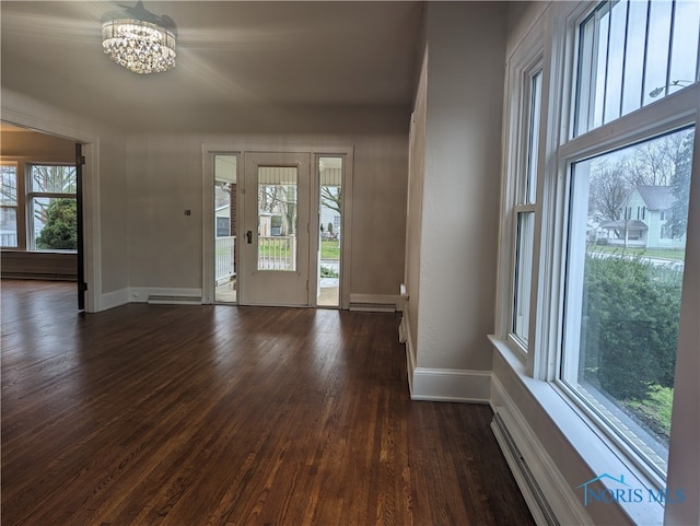 foyer with a healthy amount of sunlight, hardwood / wood-style floors, a baseboard radiator, and an inviting chandelier