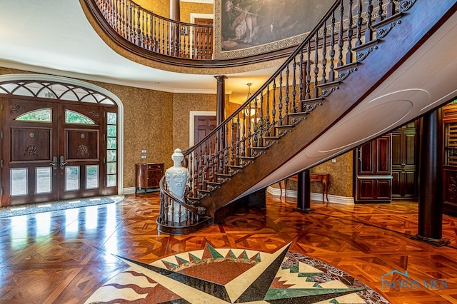 foyer featuring ornate columns, french doors, a towering ceiling, parquet floors, and crown molding