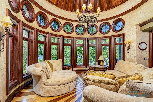 living area featuring a towering ceiling, a healthy amount of sunlight, an inviting chandelier, and hardwood / wood-style flooring