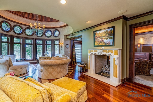 living room with dark wood-type flooring, a textured ceiling, a chandelier, ornamental molding, and a fireplace