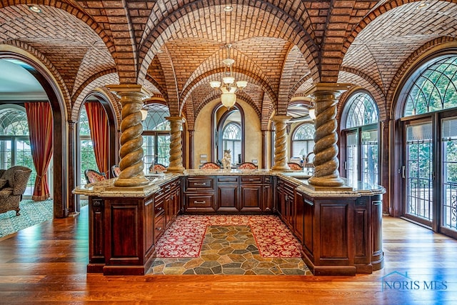 bar with hardwood / wood-style floors, brick ceiling, decorative columns, and light stone countertops