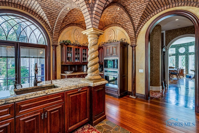 kitchen featuring sink, appliances with stainless steel finishes, light stone countertops, dark hardwood / wood-style floors, and ornate columns