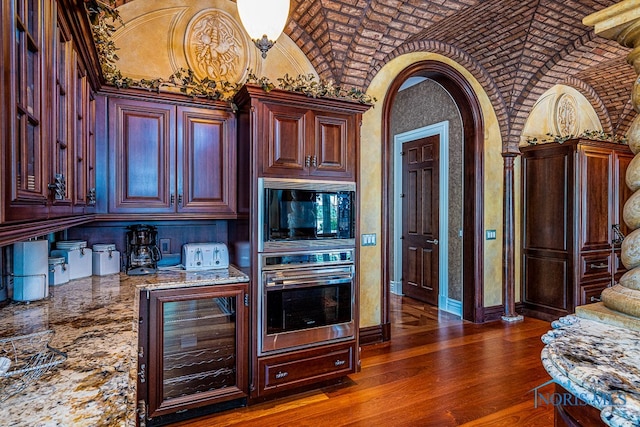 kitchen featuring stone countertops, stainless steel double oven, beverage cooler, brick ceiling, and dark hardwood / wood-style flooring