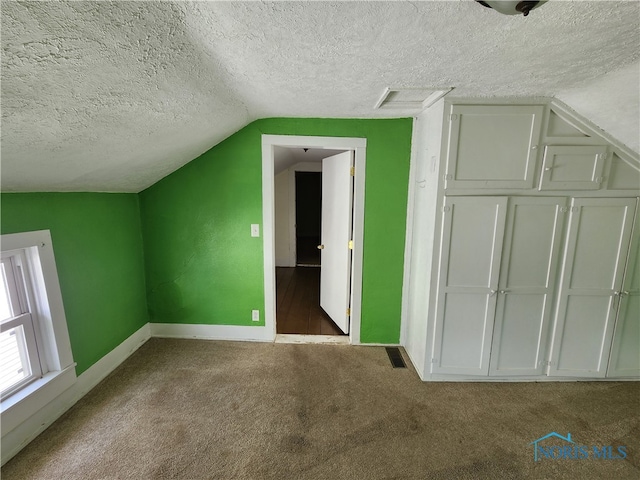 additional living space with a textured ceiling, dark carpet, and vaulted ceiling