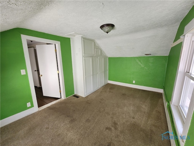 additional living space with a textured ceiling, dark colored carpet, and vaulted ceiling