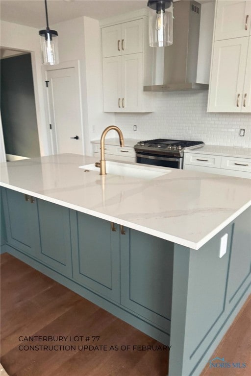 kitchen featuring stainless steel gas stove, wall chimney range hood, white cabinetry, and hanging light fixtures