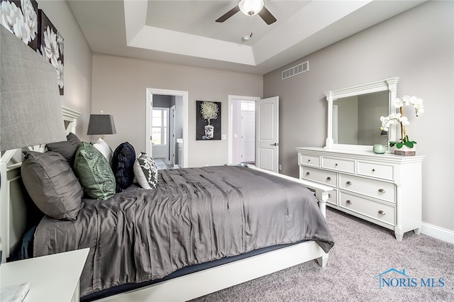 bedroom featuring carpet, ensuite bathroom, a raised ceiling, and ceiling fan