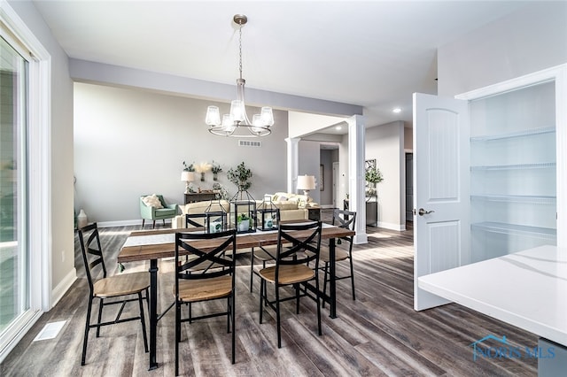 dining area featuring decorative columns, dark wood-type flooring, and an inviting chandelier