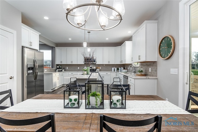 kitchen featuring decorative backsplash, stainless steel appliances, an inviting chandelier, white cabinetry, and hanging light fixtures