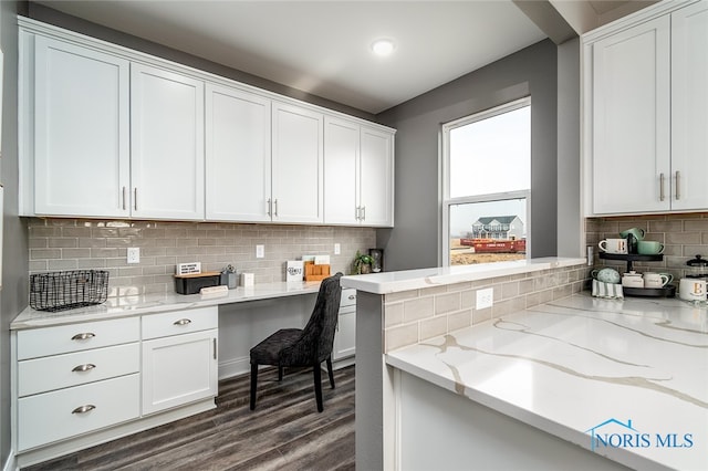 kitchen with white cabinetry, tasteful backsplash, light stone counters, dark hardwood / wood-style floors, and built in desk