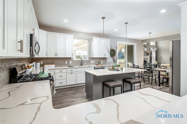 kitchen with light stone countertops, a kitchen bar, stainless steel appliances, decorative light fixtures, and a center island