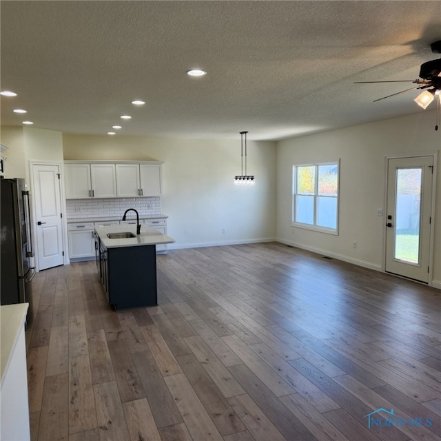 kitchen with dark wood-type flooring, an island with sink, pendant lighting, white cabinets, and stainless steel refrigerator