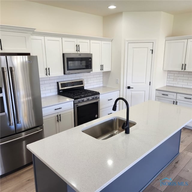 kitchen featuring sink, appliances with stainless steel finishes, a kitchen island with sink, and light hardwood / wood-style floors