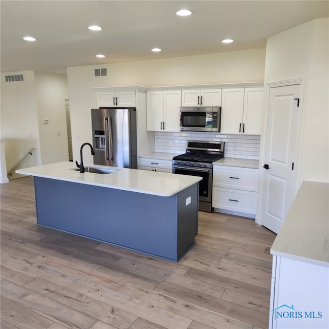 kitchen with appliances with stainless steel finishes, sink, light hardwood / wood-style floors, white cabinets, and a center island with sink