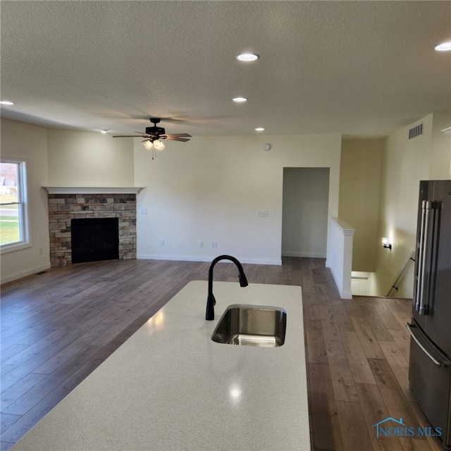 kitchen featuring sink, high end fridge, a stone fireplace, a textured ceiling, and dark hardwood / wood-style floors