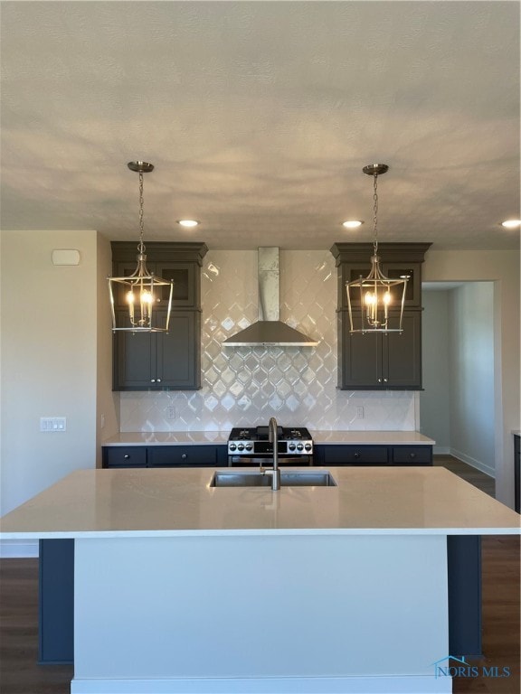 kitchen featuring wall chimney exhaust hood, an island with sink, and decorative light fixtures