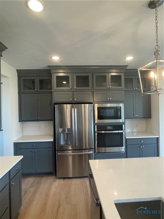 kitchen with a textured ceiling, decorative light fixtures, backsplash, appliances with stainless steel finishes, and light hardwood / wood-style floors